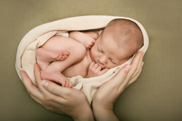 sleeping newborn boy in green winding. 
sleeping newborn boy in a green winding. the hands of the parents are holding the baby