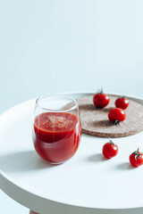 Tomato juice in glass and tomatoes on a white coffee table.