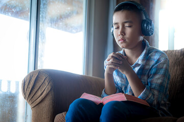 a boy learning bible and praying on sofa at home, listening to the voice of God, religion concept.