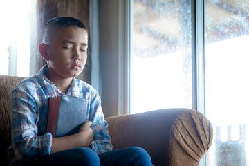 a boy embrace bible and praying on sofa at home, religion concept.