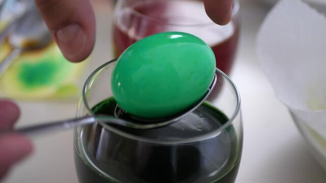 Man taking colorful egg out of a cup with green pigment