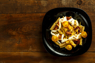 Pasta with chicken and cheese in a black plate on a wooden table.