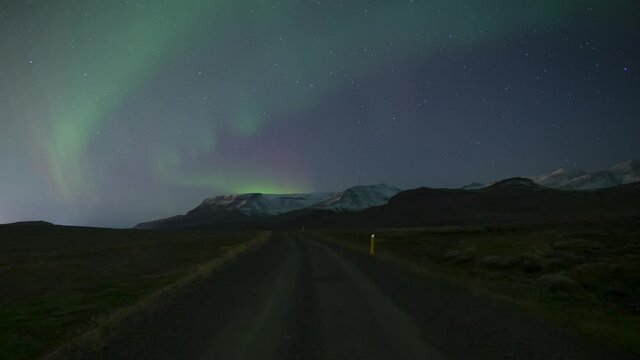 Aurora borealis over dirt road toward snow capped moutains in Iceland