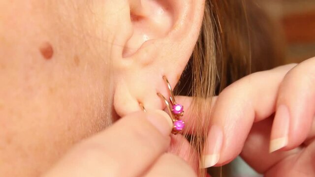 A young woman puts a gold earring in her ear. Close up.
