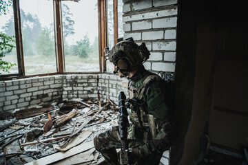 Military man with assault rifle standing inside building, he is ready for combat