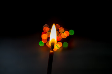 A candle is burning in the dark with blurred lights behind
