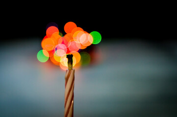 The candle burns with blurred lights in the background