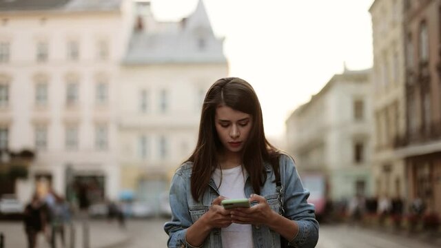 Woman looking up at street signs and map trying to find her way using her mobile phone. Young woman with dark hair using map application outdoors