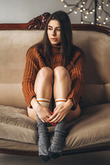 Obraz premium Pretty brunette girl in sweater and lingerie relaxing on the couch indoors.