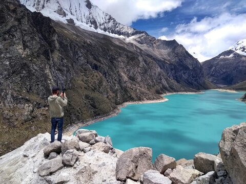 Man at Laguna Paron, Huaraz, Peru. A blue-green lake in the Cordillera Blanca on the Peruvian Andes. At 4185 meters above sea level, it's surrounded by snowy peaks and a pyramid mountain. 