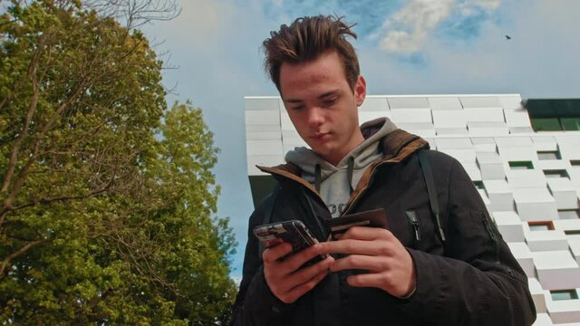 Young guy, teenager. Makes your first purchase online. Male customer holding credit card and smartphone, on modern home background. Happy boy shoppers using instant simple mobile payments while