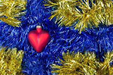 Christmas toy in the form of heart on a background of blue, red and yellow tinsel. It looks like a...