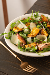 Light autumn salad with arugula, baked pumpkin, prosciutto and young parmesan, a plate of salad on a wooden table