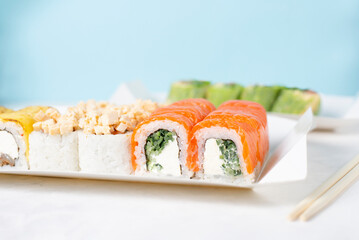Food delivery, takeaway concept. Lunch box with sushi set. Assorted sushi, Philadelphia roll, cheese, with squid on white light background. Copy space. Tasty vegetarian lunch, Japanese cuisine seafood