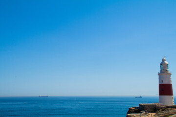 Landscape of a red and white lighthouse on a cliff with the ocean in the background