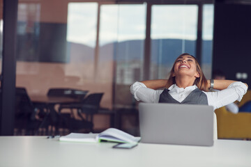 Time to relax. Cheerful young beautiful woman keeping hands behind head while sitting at her working place