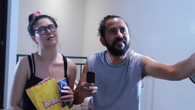 Pareja de novios casados comiendo palomitas viendo televisi&oacute;n pel&iacute;cula en casa terror miedo