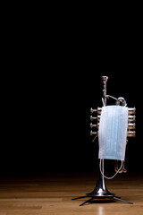 A silver plated piston piccolo trumpet with a medical mask on, to represent restrictions on...