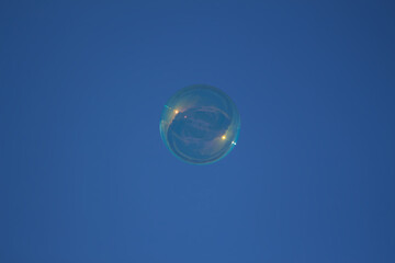 flying soap bubble with reflective rays of the sun on a blue sky background