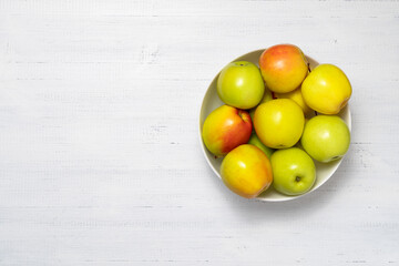 Yellow ripe apples  in the white ceramic bowl on white wood background. Top view. Copy space.