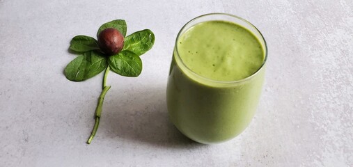 An avocado spinach smoothie alongside a flower made out of an avocado pit and fresh spinach leaves