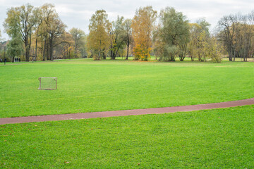 Beautiful autumn landscape. Spacious soccer field with green grass, surrounded by a running track and autumn colored forest. One-goal game concept.