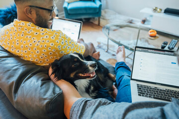 Happy gay couple working from home with laptops on couch with their Australian Shepherd 