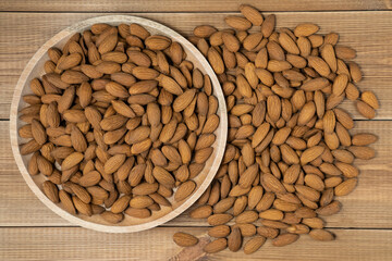 Peeled almonds nuts in bowl on wooden table, top view.