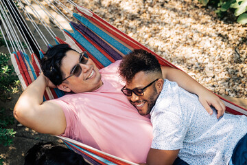 Gay couple snuggling and laughing together in hammock in back yard