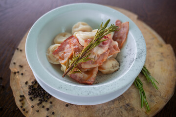 Boiled prepared homemade russian pelmeni, dumplings, ravioli with bacon on white plate with pepper, wooden rustic background. Top view.