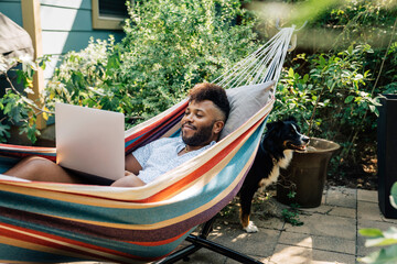 Man relaxing in hammock working on laptop computer 