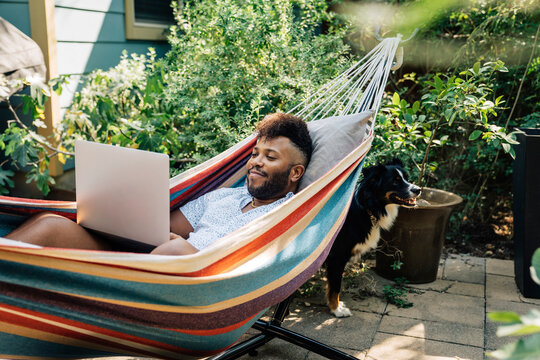 Man relaxing in hammock working on laptop computer 