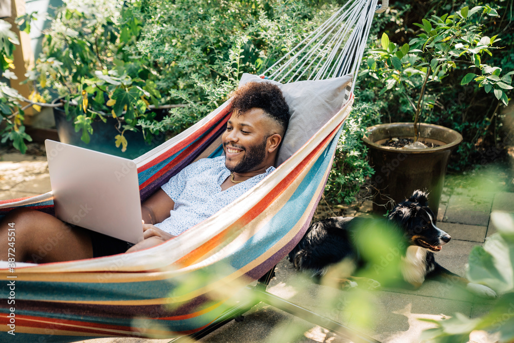 Wall mural man relaxing in hammock working on laptop computer