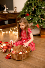 Cute little girl in red dress dresses up christmas tree at home