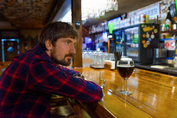 A man sits alone at the bar and drinks alcohol. Sad depressed drunk guy suffering from alcohol abuse, alcoholism concept.