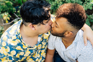 Latinx man hugging and kissing black boyfriend in garden