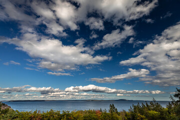 Obraz premium Soaring clouds over the ocean of Frenchman's Bay and the area surrounding Schooner Head Overlook in Acadia National Park, Maine