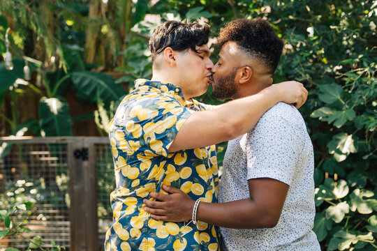 Latinx man hugging and kissing black boyfriend in garden