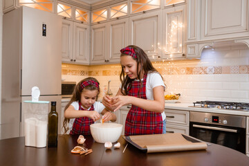 Two little girls cook at home in the kitchen ginger cookies for Christmas