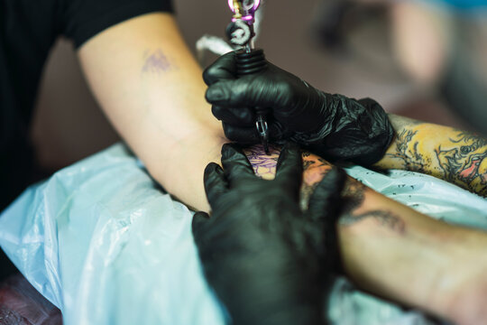 Chica joven con gafas tatuando a chico joven un dragon en el brazo