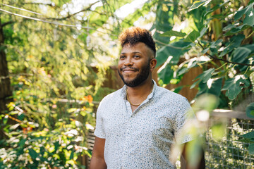 Portrait of smiling, happy confident black man with mohawk standing outdoors in garden