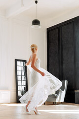 The bride is of European appearance, the blonde is whirling or dancing in a wedding dress. Full-length photograph indoors.