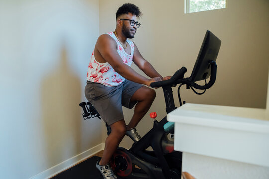 Man Working Out At Home On Stationary Bike To Cycling Class On Monitor Screen