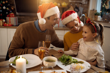 Happy parents and their small daughter having fun at dining table on Christmas.