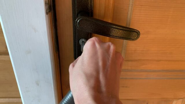 A hand holding a key and inserting it in a keyhole, unlocking and opening a white wooden door, home security and protection concept