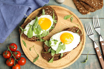 Delicious sandwiches with arugula and fried egg on blue wooden table, flat lay