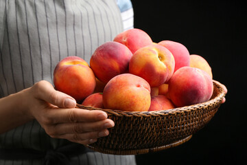Woman with fresh sweet peaches in wicker bowl, closeup