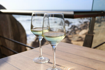 Two glasses of white wine on a table overlooking the ocean.