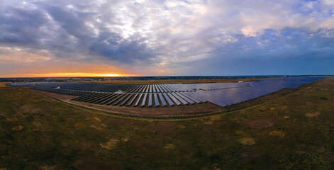 Aerial panorama view into large solar panels at a solar farm at bright sunset. Solar cell power plants.