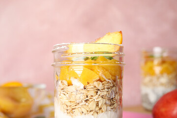 Tasty peach dessert with yogurt and granola on pink background, closeup